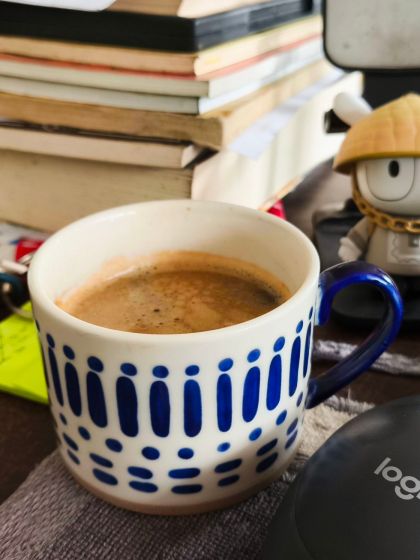 A cup of coffee, on a desk with books and papers.
