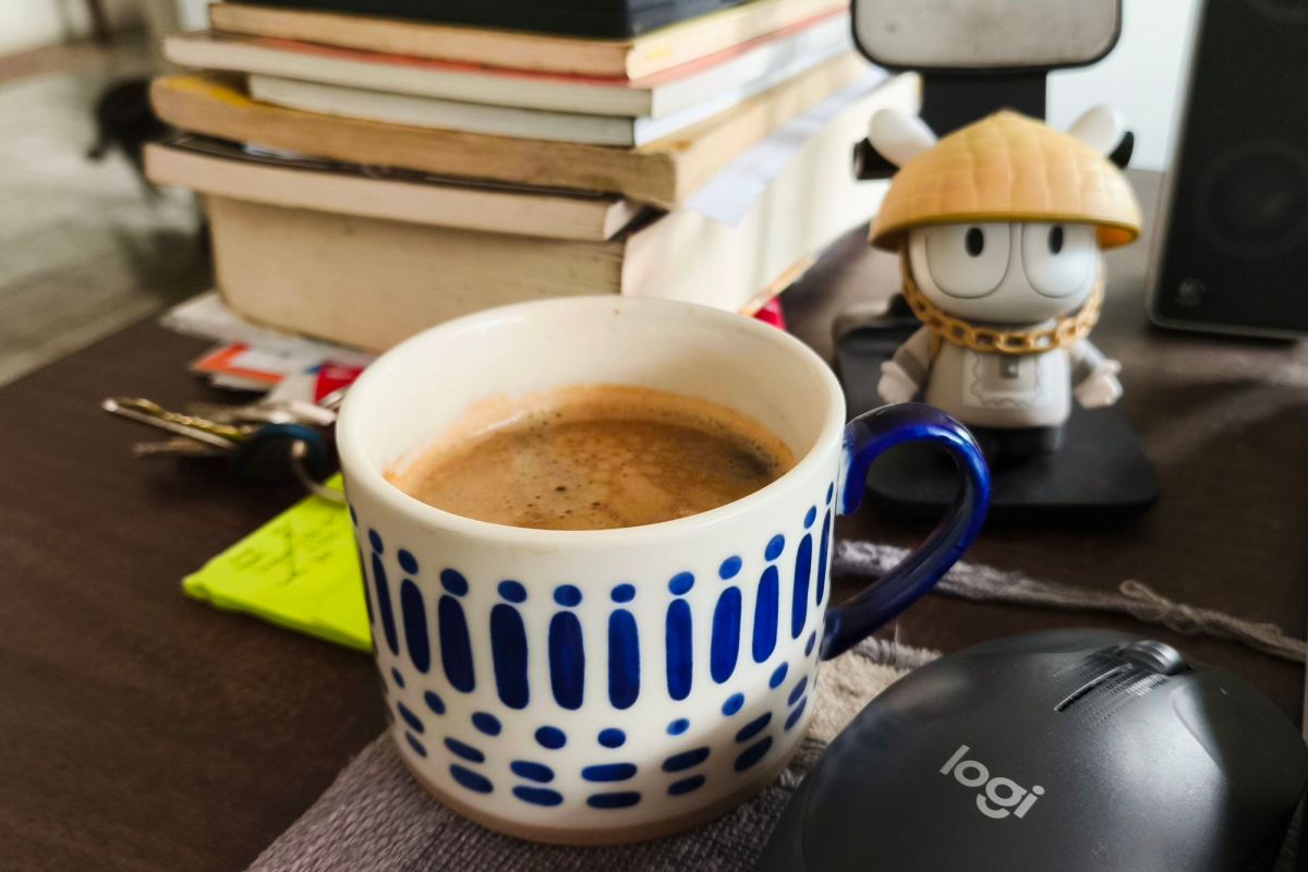A cup of coffee, on a desk with books and papers.