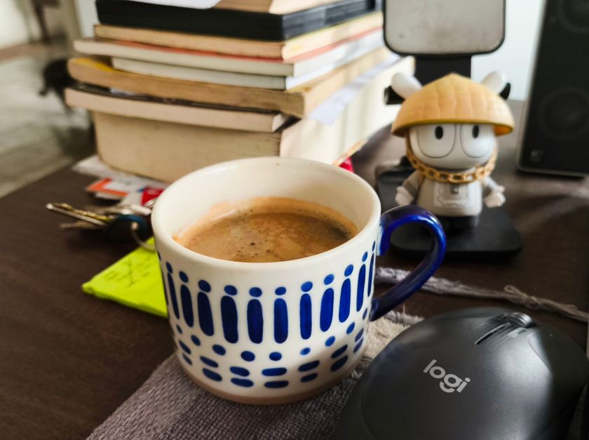 A cup of coffee, on a desk with books and papers.